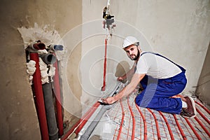 Male worker installing underfloor heating system in apartment.