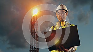 Male worker with a laptop near the oil refinery pipes