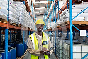 Male worker looking at camera while writing on clipboard in warehouse