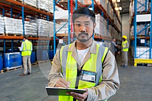 Male worker looking at camera while writing on clipboard in warehouse