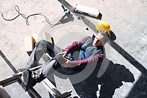 Male worker lying on the floor after fall from ladder, holding his knee. Work injury, accident in workplace.