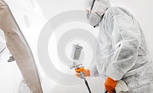 Male worker with mask and protective clothes painting car using spray compressor.