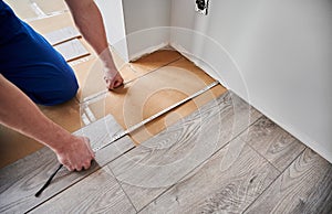 Male worker measuring distance from wall to laminate plank.