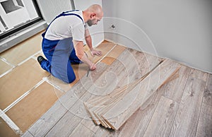 Male worker measuring distance from wall to laminate wood plank.