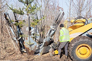 Male worker operates tree transplanter heavy machine. Landscaping, seasonal agricultural engineering, large trees landing machines