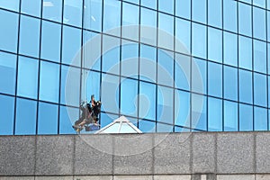 Male worker in overalls professional repair the windows in high-rise. Worker washing windows in office building. Washer wash the