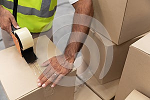 Male worker packing cardboard box with tape gun dispenser in warehouse