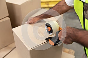 Male worker packing cardboard box with tape gun dispenser in warehouse