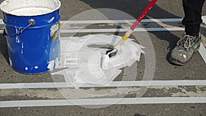 Male worker painting white marking line of disabled parking lot sign on asphalt