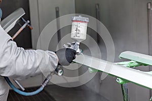 A male worker paints with a spray gun a part of the car body in silver after being damaged at an accident. Plastic elements from