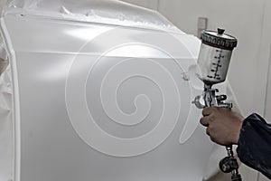 A male worker paints with a spray gun a part of the car body in photo