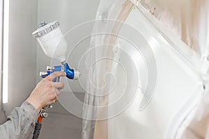 A male worker paints with a spray gun a part of the car body in white after being damaged at an accident. Door from the vehicle