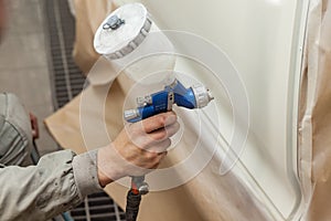 A male worker paints with a spray gun a part of the car body in white after being damaged at an accident. Door from the vehicle