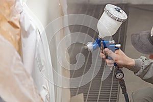 A male worker paints with a spray gun a part of the car body in white after being damaged at an accident. Door from the vehicle