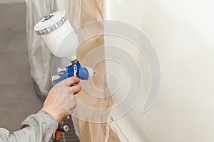 A male worker paints with a spray gun a part of the car body in white after being damaged at an accident. Door from the vehicle