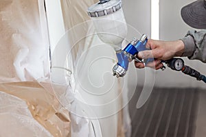 A male worker paints with a spray gun a part of the car body in white after being damaged at an accident. Door from the vehicle