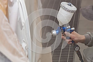 A male worker paints with a spray gun a part of the car body in white after being damaged at an accident. Door from the vehicle