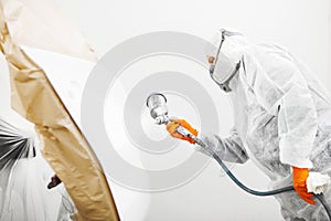 Male worker in protective clothes and mask painting car using spray paint.