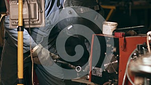 Male worker in protective glowes welds two metal pieces together at mechanical hangar.