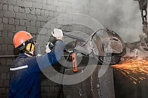 A male worker in a protective helmet, respirator, overalls manages heavy grinding equipment for cast iron concrete tubing with