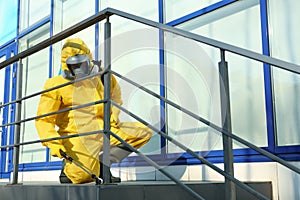 Male worker in protective suit spraying insecticide on stairs. Pest control