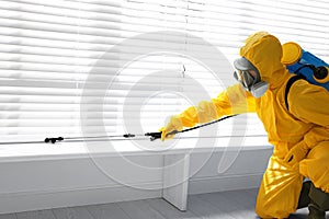 Male worker in protective suit spraying insecticide on window sill. Pest control