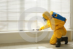 Male worker in protective suit spraying insecticide on window sill, space for text. Pest control