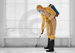 Male worker in protective suit spraying insecticide on wooden floor, space for text. Pest control