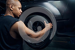 Male worker putting on and attaching wheels to a new car