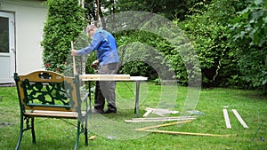 Male worker renewing old outdoor furniture bench. Man polishing wood boards