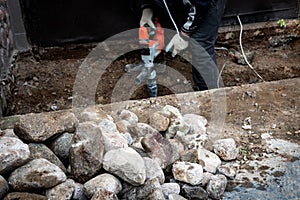 Male worker repairing driveway surface with jackhammer, digging and drilling concrete road