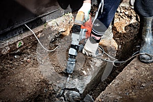 Male worker repairing driveway surface with jackhammer, digging and drilling concrete road