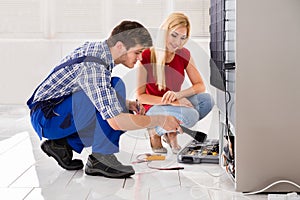 Male Worker Repairing Refrigerator In Kitchen Room