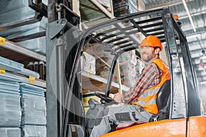 male worker in safety vest and helmet sitting in forklift machine