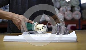 Male worker on a sewing manufacture uses electric cutting fabric machine with chain glove