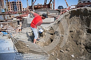 Male worker shoveling sand-cement mix at construction site.
