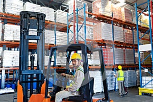 Male worker sitting in forklift and looking at camera in warehouse