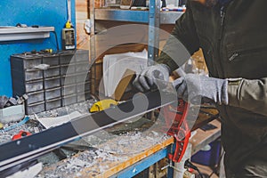 A male worker in a ski service workshop repairs the sliding surface of the skis. Close-up of a hand with a plastic scrapper for