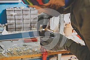 A male worker in a ski service workshop repairs the sliding surface of the skis. Close-up of a hand with a plastic scrapper for re