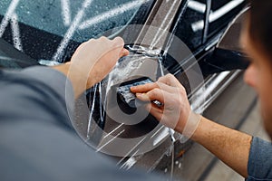 Male worker smoothes car protection film, tuning