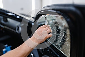 Male worker with squeegee wipes car tinting photo