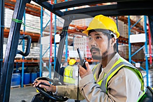 Male worker talking on walkie-talkie while driving forklift in warehouse