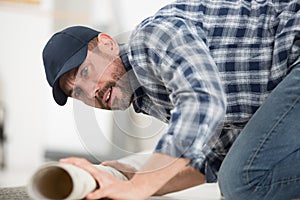 Male worker unrolling carpet on floor at home