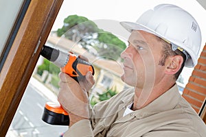 male worker using cordless drill on window