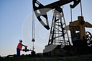 Male worker using petroleum pump jack in oil field.