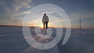 Male worker in warm clothes and warm boots goes on a cold winter day in the snow along the power line