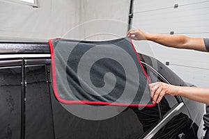 A male worker washes a black car, wiping water with a soft cloth and microfiber, cleaning the surface to shine in a vehicle