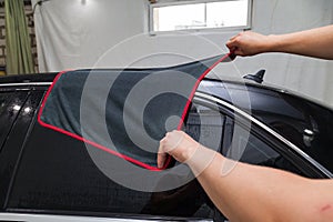 A male worker washes roof of a black car, wiping water with a soft cloth and microfiber, cleaning the surface to shine in a