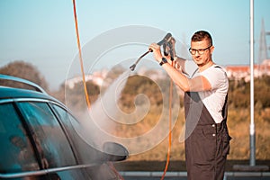Male worker washing car in a car wash station using high pressure water