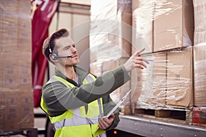 Male Worker Wearing Headset At Freight Haulage Business With Truck Being Loaded By Fork Lift 